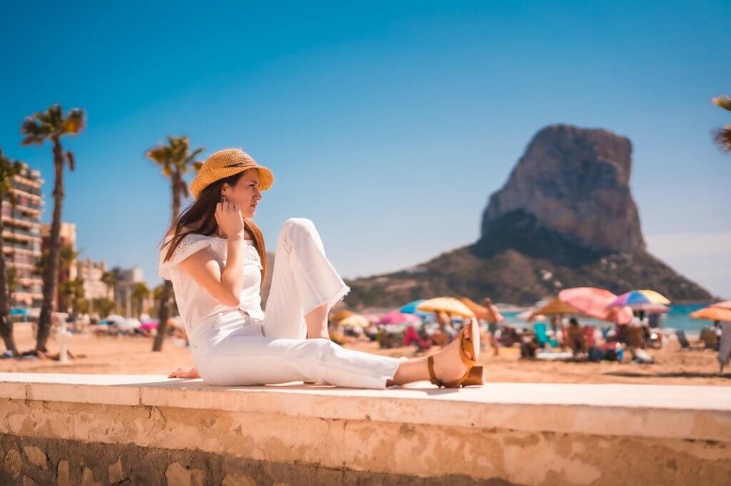 A Caucasian redhead dressed in white and with a straw hat on the beaches of Calpe