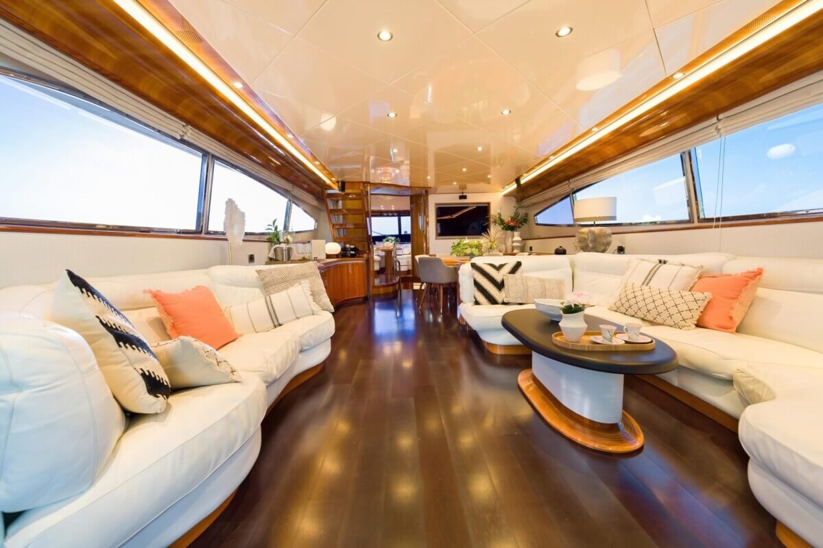 Interior de salón de un yate de lujo, con muebles elegantes y grandes ventanales, mostrando el confort que ofrece el alquiler de yates de lujo Ibiz